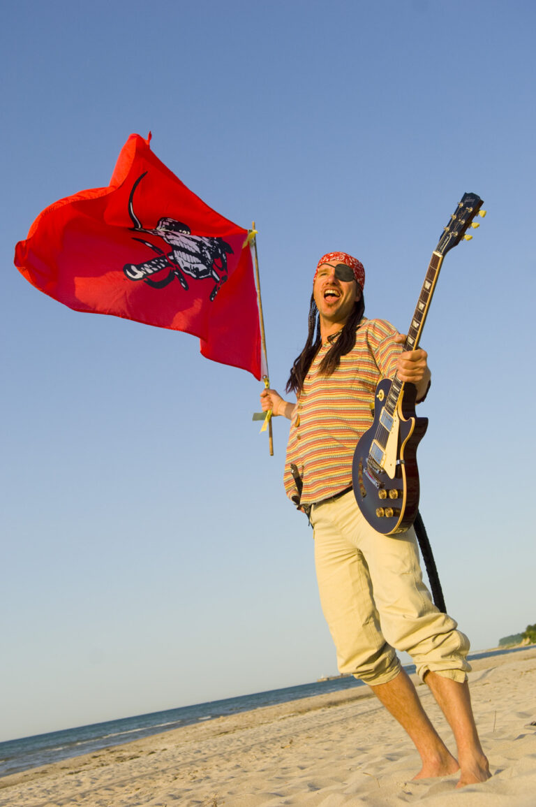 Spooky Der Steuermann schwenkt die Piraten Fahne kurz vor Konzert Beginn am Strand mit einer Gibson Gitarre.